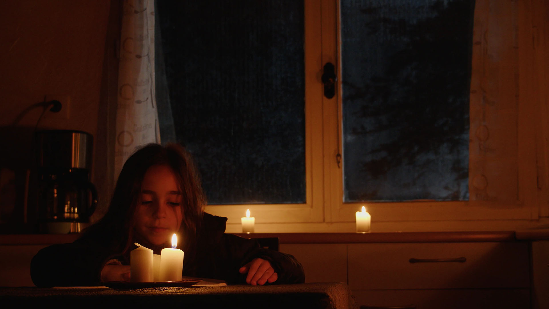 Une petite fille assise en train de faire ses devoirs dans une pièce très sombre Fille Maison